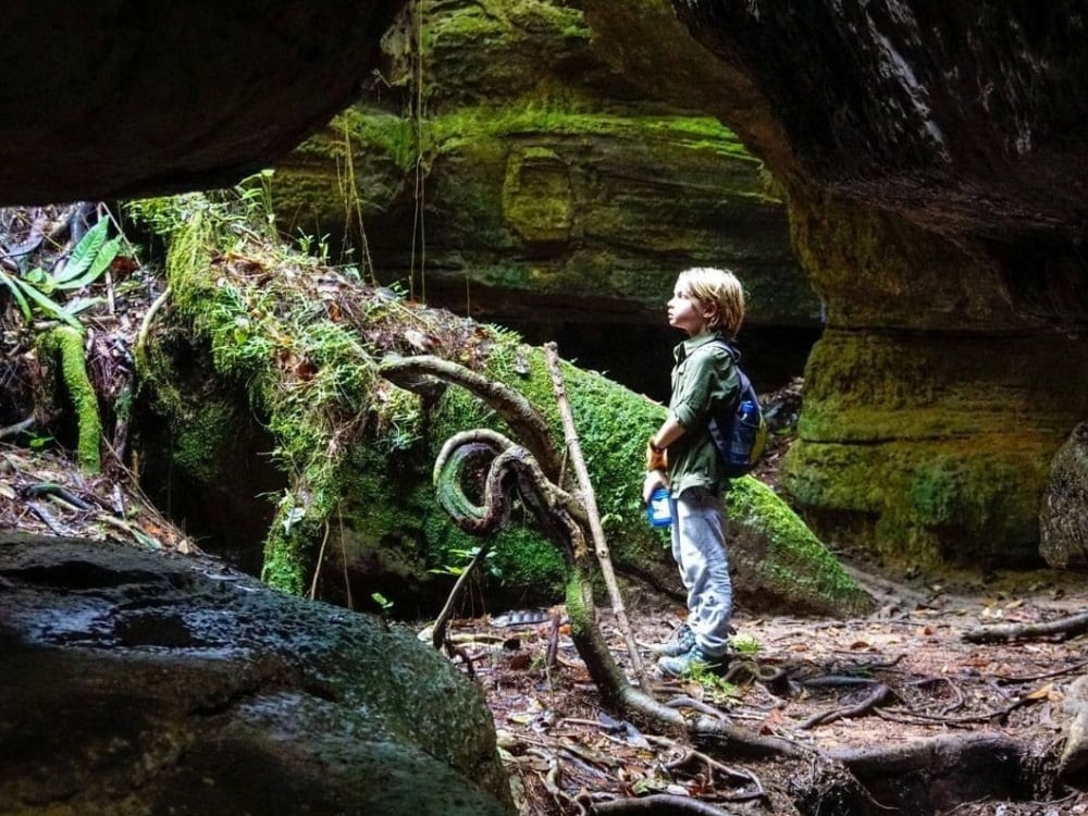 Kleiner Junge steht am Eingang einer moosigen Höhle und erkundet den Amazonas-Dschungel. Kleiner Junge steht am Eingang einer moosigen Höhle und erkundet den Amazonas-Dschungel.