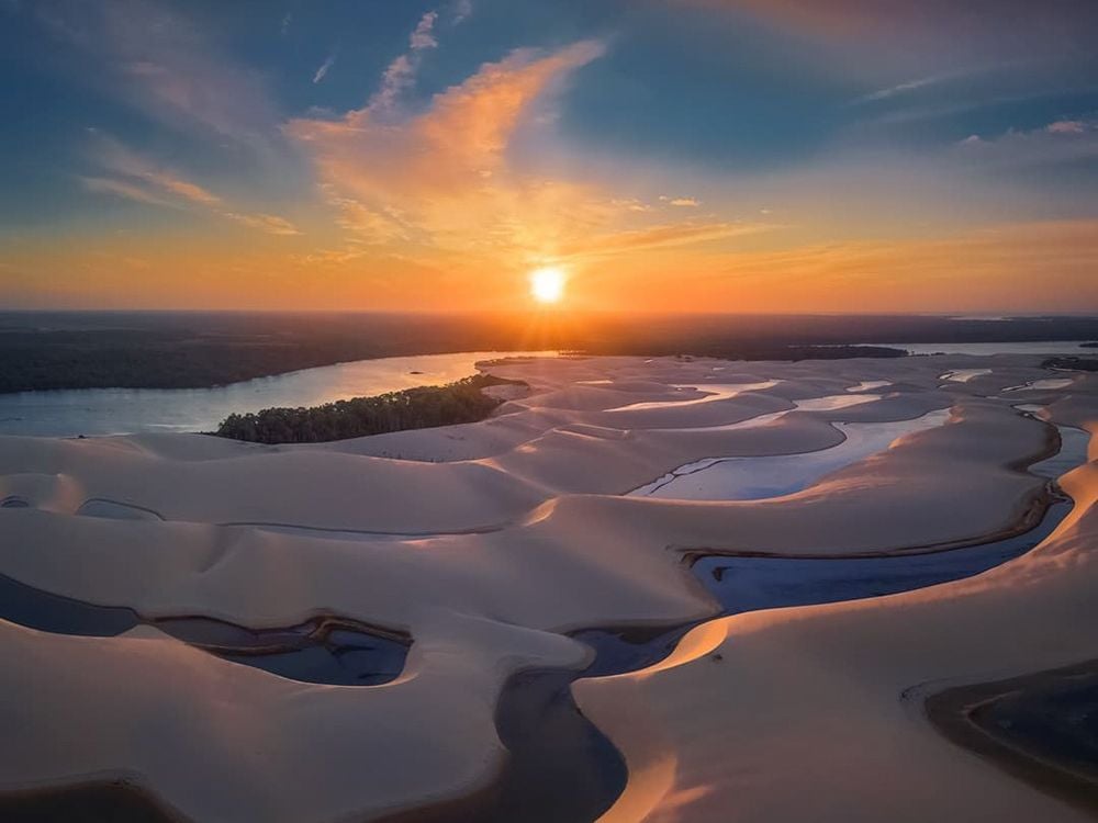 Vista aérea das dunas do Brasil com canais de água sinuosos refletindo a luz dourada de um pôr do sol vibrante no Parque Nacional Lençóis Maranhenses. Vista aérea das dunas do Brasil com canais de água sinuosos refletindo a luz dourada de um pôr do sol vibrante no Parque Nacional Lençóis Maranhenses.