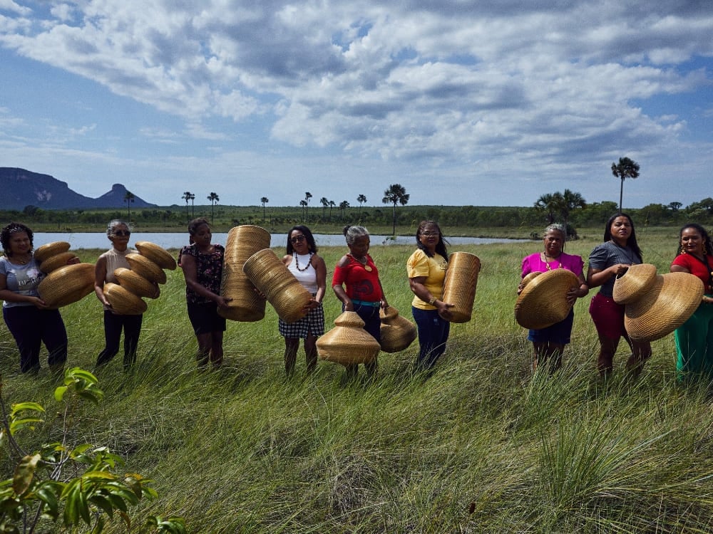 Un groupe de femmes debout dans un champ verdoyant sous un ciel nuageux, brandissant des objets artisanaux tressés en herbe dorée dans la région du Jalapão Un groupe de femmes debout dans un champ verdoyant sous un ciel nuageux, brandissant des objets artisanaux tressés en herbe dorée dans la région du Jalapão
