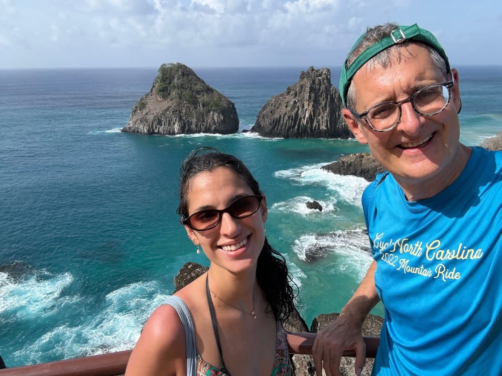 Vater und Tochter lächeln für ein Selfie an einem Aussichtspunkt mit Blick auf den türkisfarbenen Ozean und die ikonischen Felsformationen Morro Dois Irmãos. Vater und Tochter lächeln für ein Selfie an einem Aussichtspunkt mit Blick auf den türkisfarbenen Ozean und die ikonischen Felsformationen Morro Dois Irmãos.