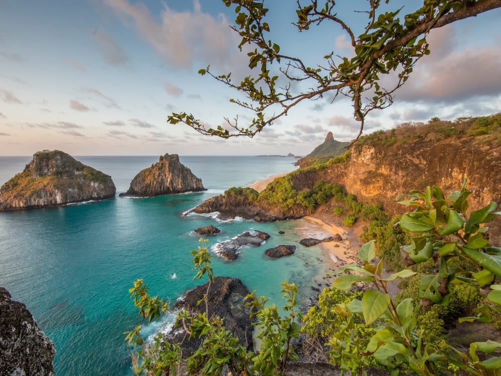 Malerischer Küstenblick auf Fernando de Noronha mit türkisfarbenem Wasser, einer Sandbucht und den Felsformationen Morro Dois Irmãos, umrahmt von grüner Vegetation. Malerischer Küstenblick auf Fernando de Noronha mit türkisfarbenem Wasser, einer Sandbucht und den Felsformationen Morro Dois Irmãos, umrahmt von grüner Vegetation.