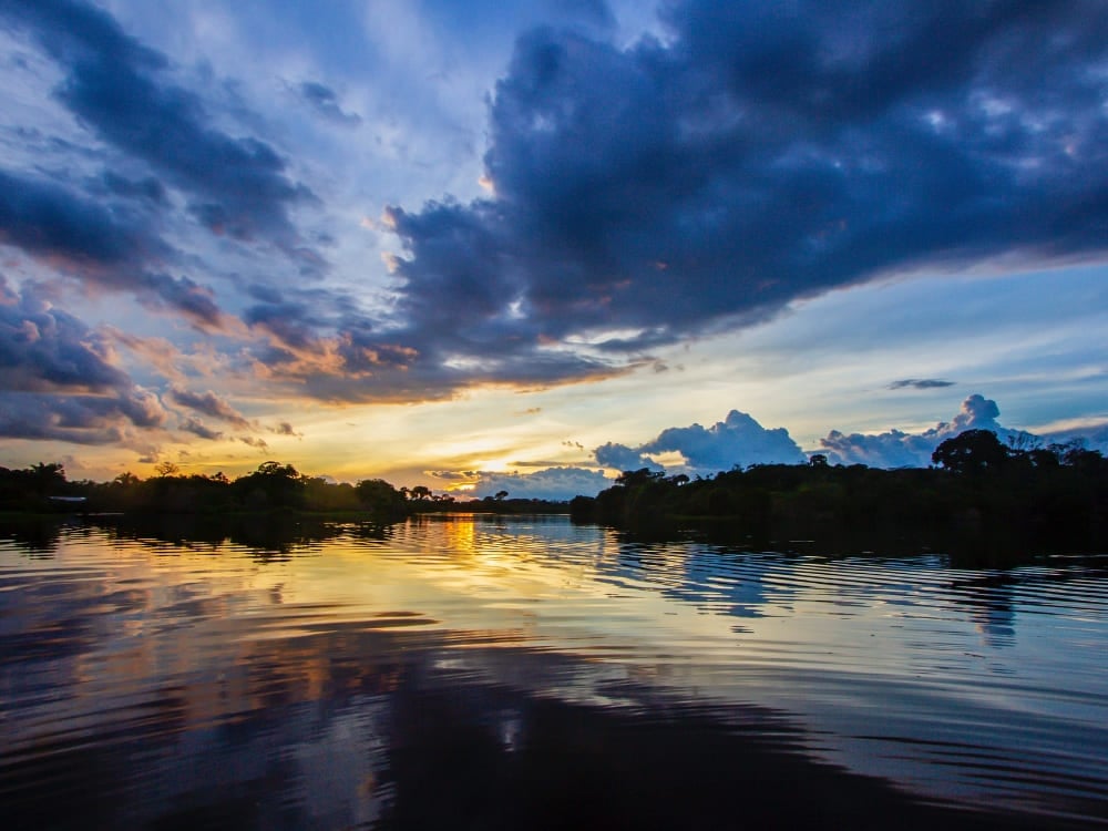 Um pôr do sol colorido refletido nas águas calmas do Rio Amazonas, cercado pela floresta. Um pôr do sol colorido refletido nas águas calmas do Rio Amazonas, cercado pela floresta.
