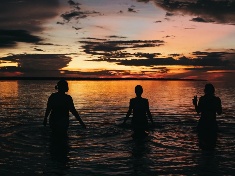 Silhuetas de três pessoas com a água pela cintura nas águas do Amazonas durante o pôr do sol. Silhuetas de três pessoas com a água pela cintura nas águas do Amazonas durante o pôr do sol.