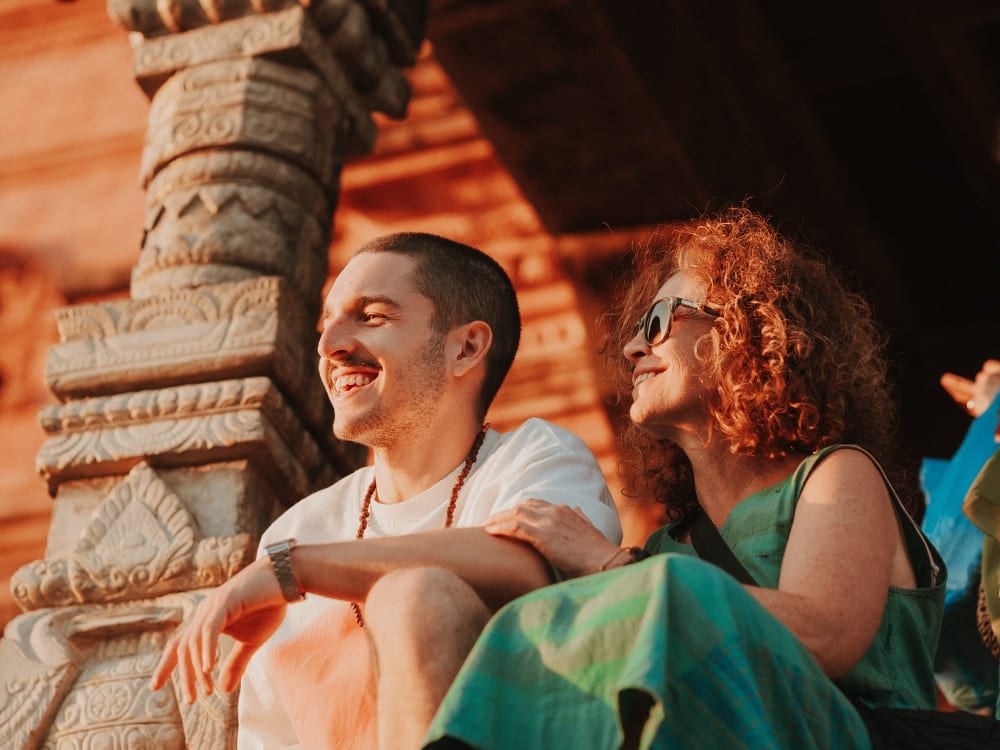 Mila Ricetti en haar zoon Lorenzo lachend en samen zittend bij een historische stenen tempel tijdens hun ecotoeristische expeditie in Nepal. Mila Ricetti en haar zoon Lorenzo lachend en samen zittend bij een historische stenen tempel tijdens hun ecotoeristische expeditie in Nepal.