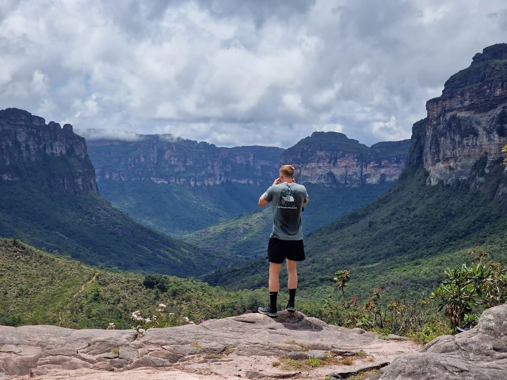 Um trilheiro de pé num afloramento rochoso fotografando os vastos vales verdes e as montanhas de topo plano. Um trilheiro de pé num afloramento rochoso fotografando os vastos vales verdes e as montanhas de topo plano.