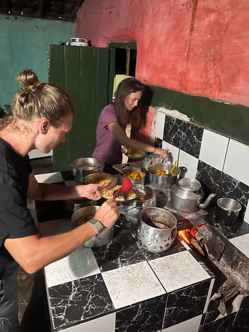 Dois trilheiros se servindo de comida fresca e caseira em várias panelas numa cozinha rústica de uma casa de família. Dois trilheiros se servindo de comida fresca e caseira em várias panelas numa cozinha rústica de uma casa de família.