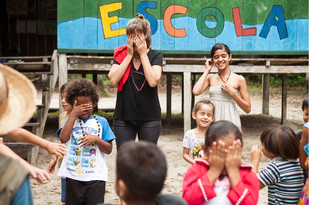 Grupo de crianças locais sorridentes e um turista interagindo em frente ao prédio de uma escola de uma comunidade ribeirinha na Amazônia. Grupo de crianças locais sorridentes e um turista interagindo em frente ao prédio de uma escola de uma comunidade ribeirinha na Amazônia.