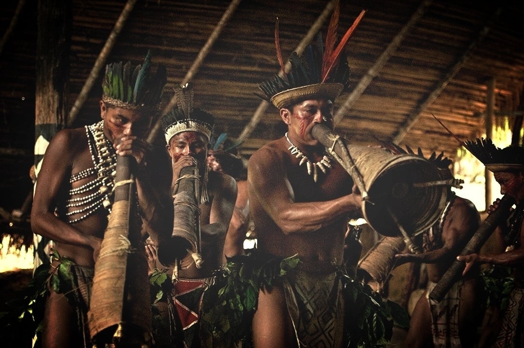 Indígenas da Amazônia tocando instrumentos de sopro tradicionais durante uma apresentação cultural. Indígenas da Amazônia tocando instrumentos de sopro tradicionais durante uma apresentação cultural.