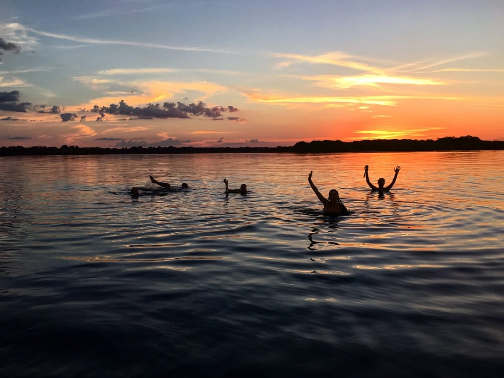 Een groep reizigers zwemt in een kalme zwartwaterrivier tijdens een levendige oranje zonsondergang. Een groep reizigers zwemt in een kalme zwartwaterrivier tijdens een levendige oranje zonsondergang.