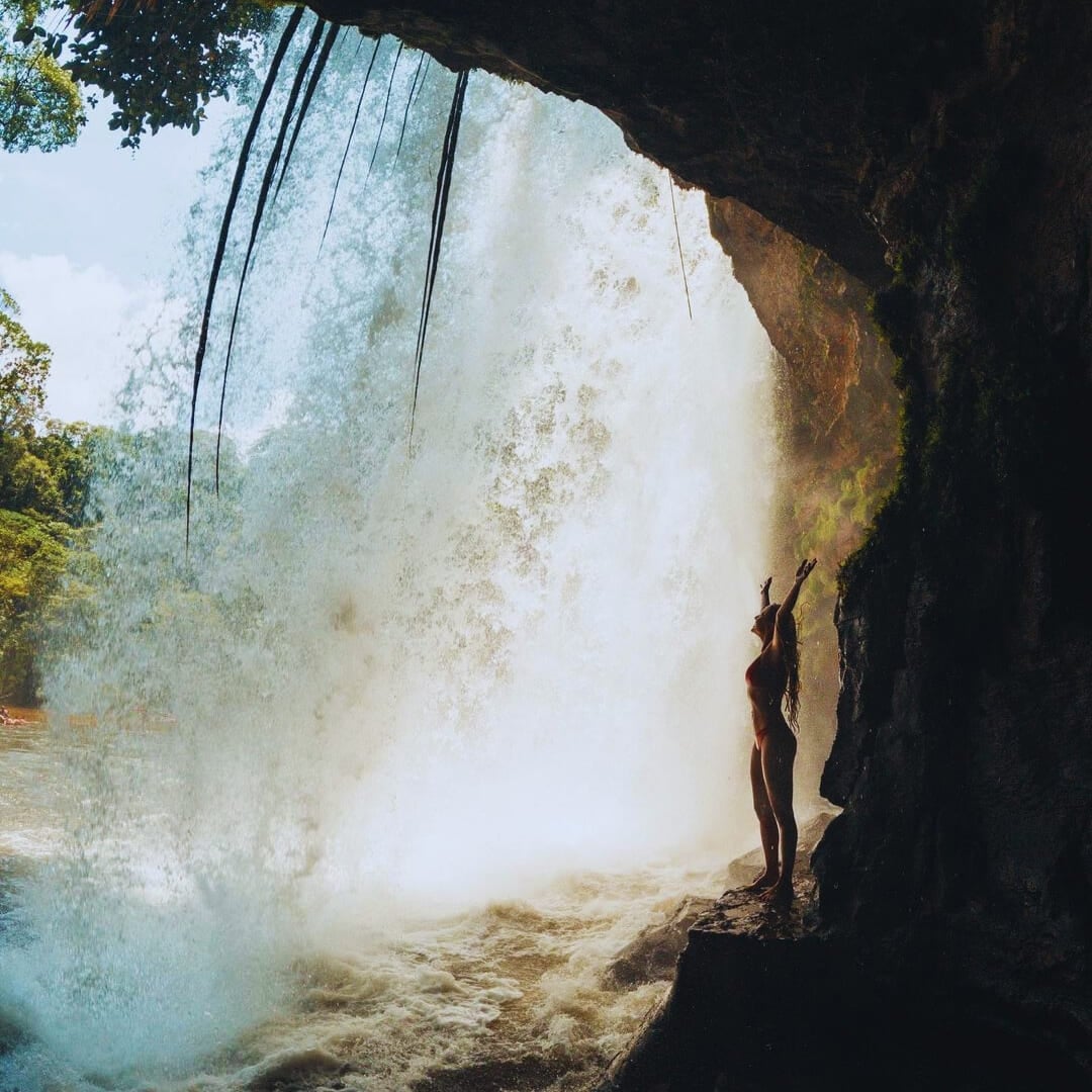 Een reiziger staat met geheven armen achter een krachtige, kletterende waterval in de jungle. Een reiziger staat met geheven armen achter een krachtige, kletterende waterval in de jungle.