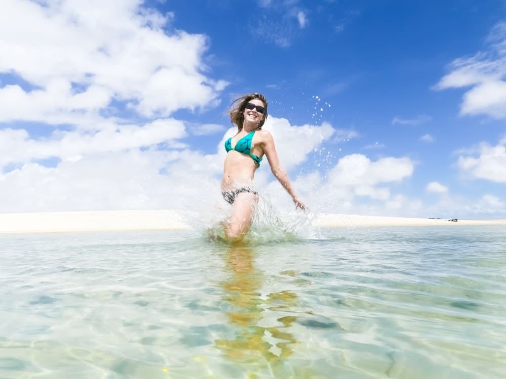 Eine lächelnde Frau genießt an einem sonnigen Tag ein erfrischendes Bad in einer kristallklaren Süßwasserlagune in den Lençóis Maranhenses. Eine lächelnde Frau genießt an einem sonnigen Tag ein erfrischendes Bad in einer kristallklaren Süßwasserlagune in den Lençóis Maranhenses.