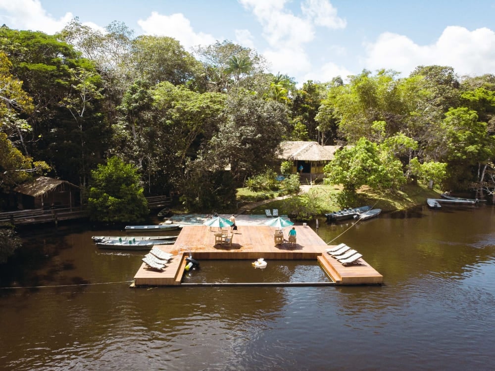 Vista aérea do Dolphin Lodge mostrando seu deck flutuante, barcos e chalés cercados pela floresta amazônica. Vista aérea do Dolphin Lodge mostrando seu deck flutuante, barcos e chalés cercados pela floresta amazônica.