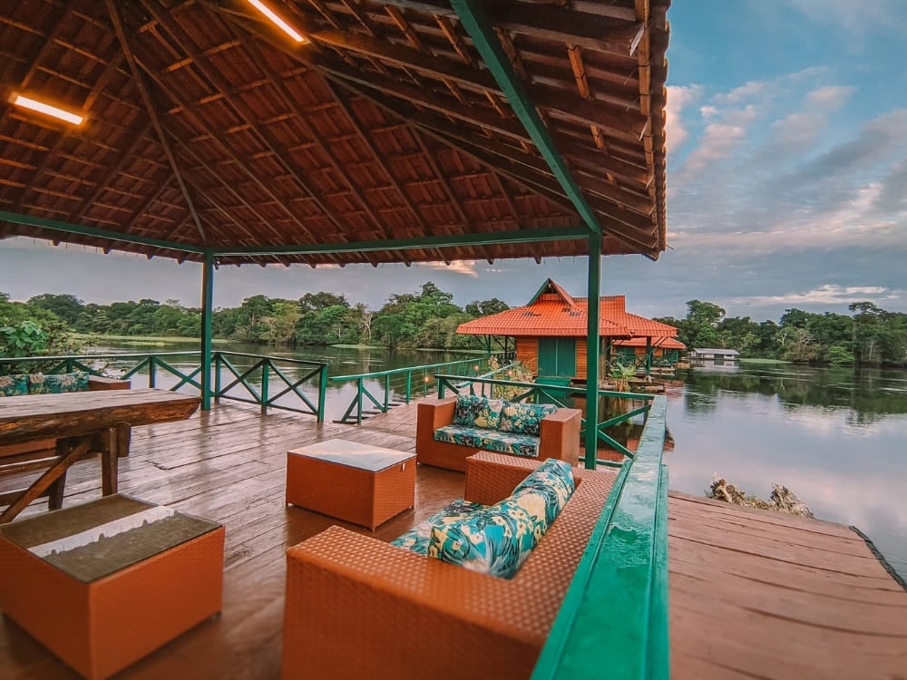 Um deck de madeira com sofás confortáveis com vista para os bangalôs flutuantes e o rio no Uakari Lodge, no Brasil. Um deck de madeira com sofás confortáveis com vista para os bangalôs flutuantes e o rio no Uakari Lodge, no Brasil.