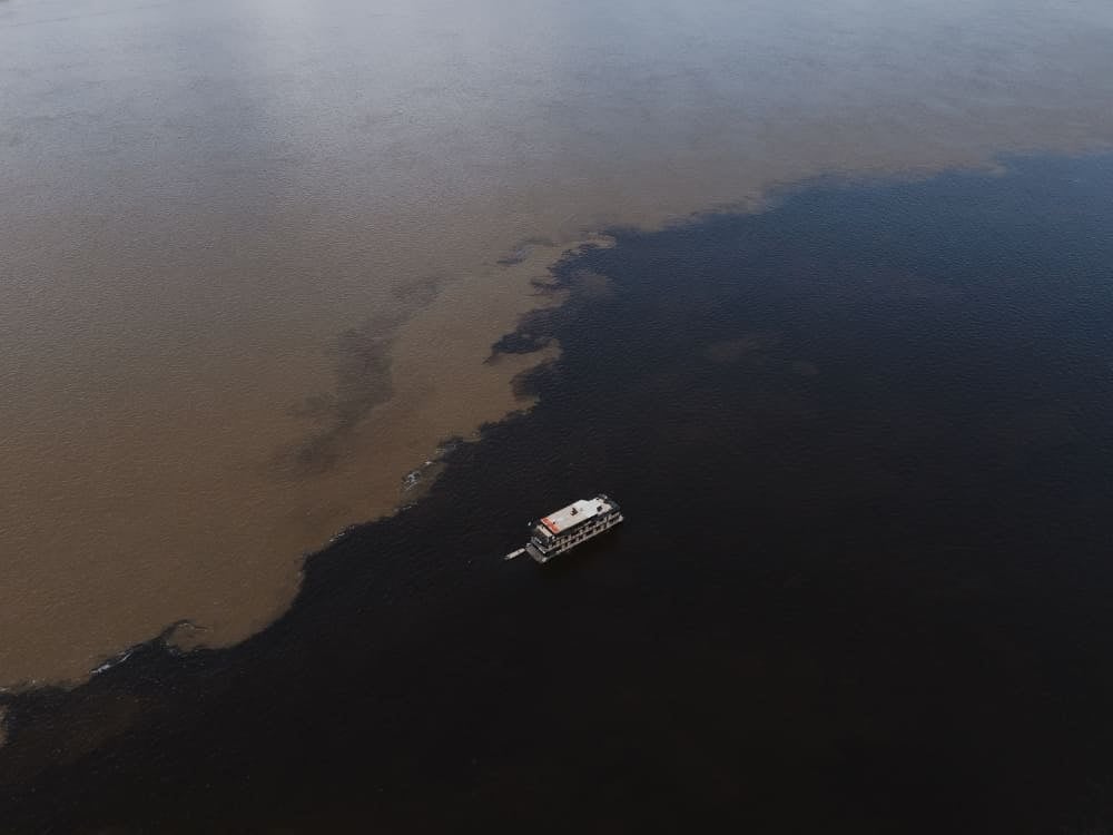 Um barco navegando no Encontro das Águas, onde o Rio Negro preto e o Rio Solimões marrom fluem lado a lado sem se misturar. Um barco navegando no Encontro das Águas, onde o Rio Negro preto e o Rio Solimões marrom fluem lado a lado sem se misturar.