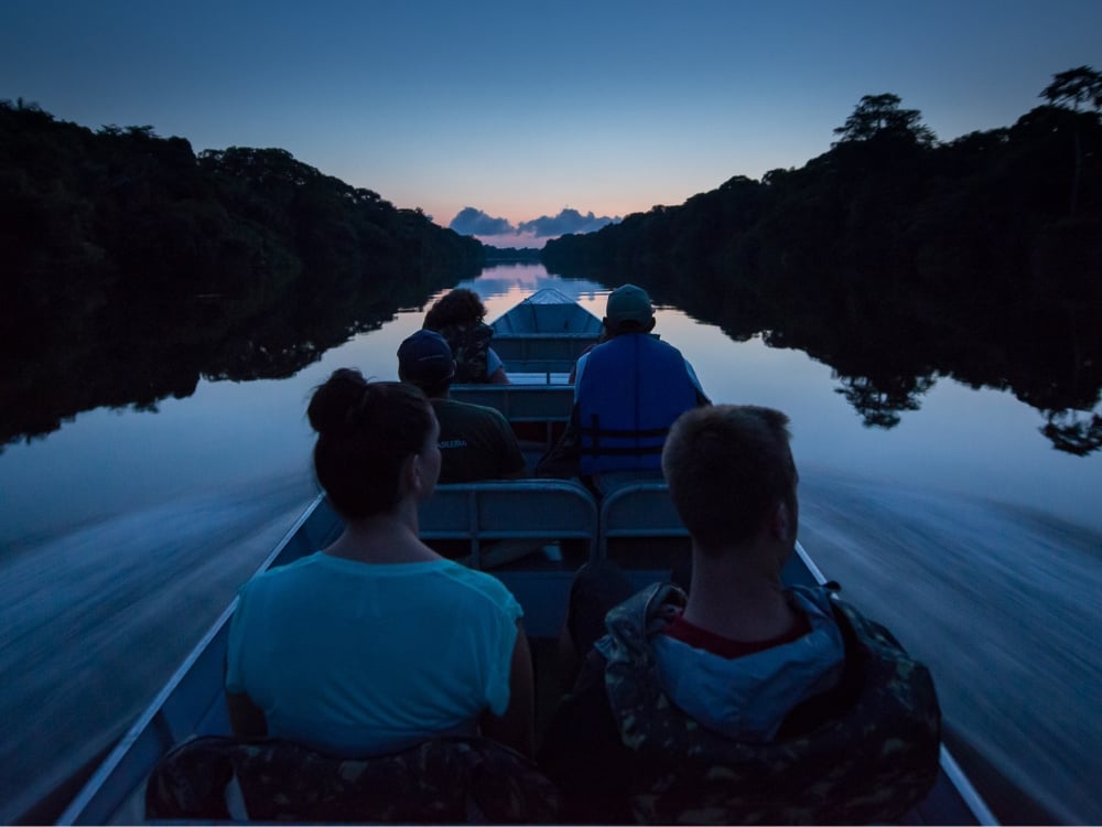 Des touristes en pirogue à moteur explorant les eaux calmes du fleuve de la forêt Amazonienne au crépuscule. Des touristes en pirogue à moteur explorant les eaux calmes du fleuve de la forêt Amazonienne au crépuscule.