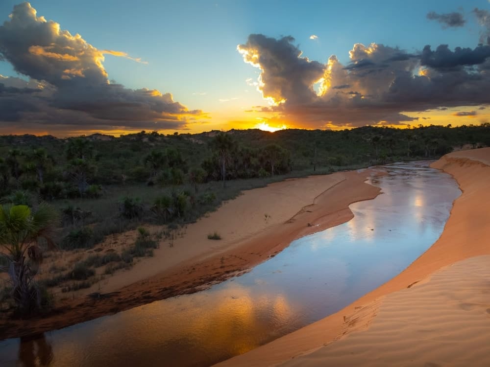 Ein ruhiger Fluss, der bei Sonnenuntergang durch weite Sandgebiete und schroffe Klippen fließt und die geologische Vergangenheit der Region widerspiegelt. Ein ruhiger Fluss, der bei Sonnenuntergang durch weite Sandgebiete und schroffe Klippen fließt und die geologische Vergangenheit der Region widerspiegelt.