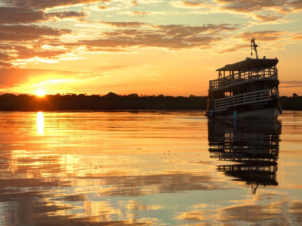 Bateau fluvial traditionnel en bois naviguant sur les eaux calmes de l'Amazonie pendant un coucher de soleil doré qui se reflète sur le fleuve. Bateau fluvial traditionnel en bois naviguant sur les eaux calmes de l'Amazonie pendant un coucher de soleil doré qui se reflète sur le fleuve.