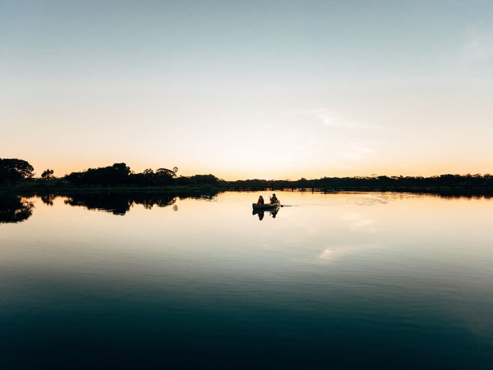 Deux personnes pagayant en canoë sur une rivière calme qui reflète le ciel dans la région du Pantanal. Deux personnes pagayant en canoë sur une rivière calme qui reflète le ciel dans la région du Pantanal.