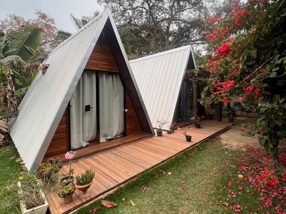 Deux chalets rustiques en bois avec des toits en pointe se dressent à Berço Pantaneiro à Porto Jofre, entourés de fleurs roses éclatantes. Deux chalets rustiques en bois avec des toits en pointe se dressent à Berço Pantaneiro à Porto Jofre, entourés de fleurs roses éclatantes.