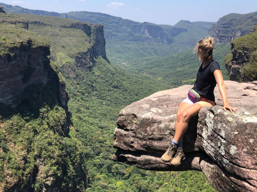 Wanderin ruht sich an einer felsigen Klippe aus und blickt während eines Ökotourismus-Abenteuers über einen weiten, üppig grünen Canyon und ferne Hochebenen. Wanderin ruht sich an einer felsigen Klippe aus und blickt während eines Ökotourismus-Abenteuers über einen weiten, üppig grünen Canyon und ferne Hochebenen.