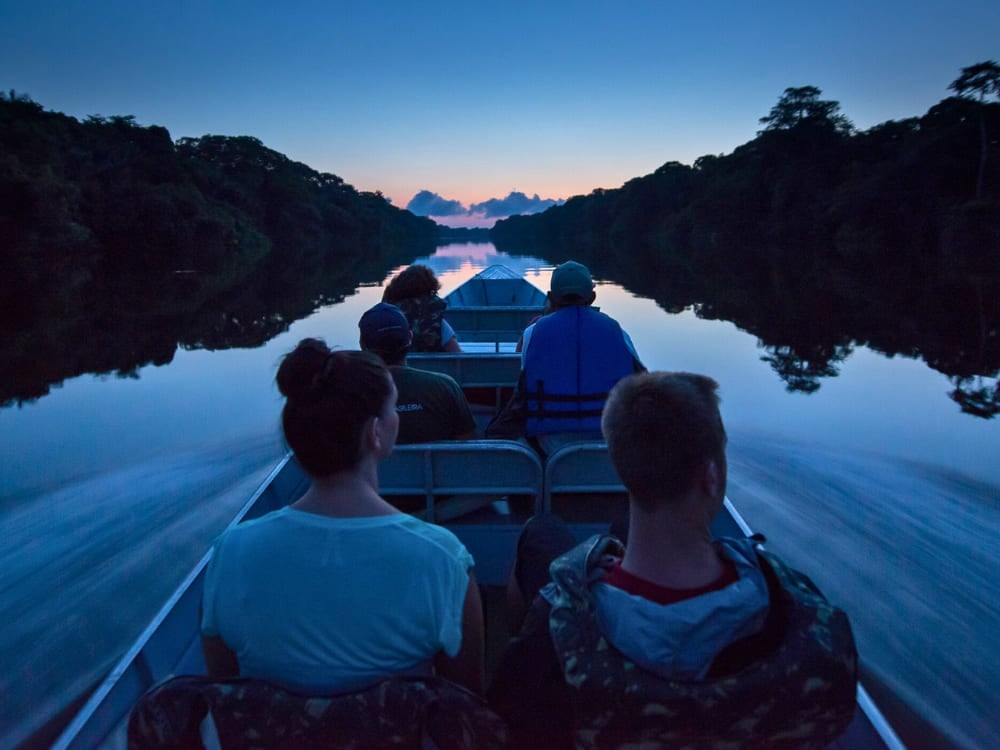 Touristen auf einem kleinen motorisierten Kanu, die in der Dämmerung einen Amazonas-Fluss befahren. Touristen auf einem kleinen motorisierten Kanu, die in der Dämmerung einen Amazonas-Fluss befahren.