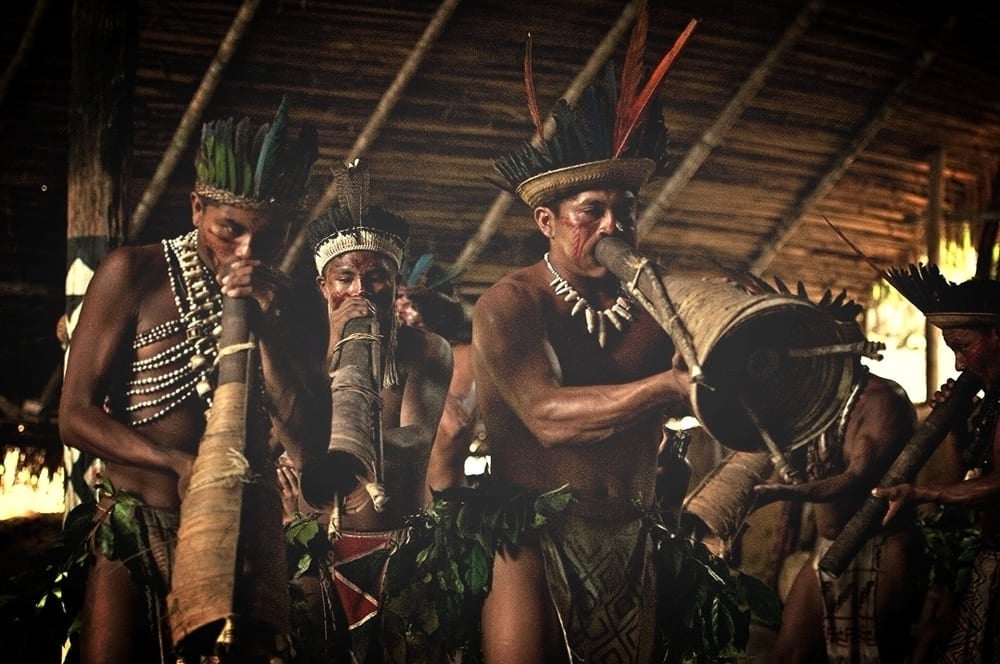 Um grupo de indígenas na Amazônia tocando instrumentos de sopro tradicionais e tambores durante um ritual cultural. Um grupo de indígenas na Amazônia tocando instrumentos de sopro tradicionais e tambores durante um ritual cultural.