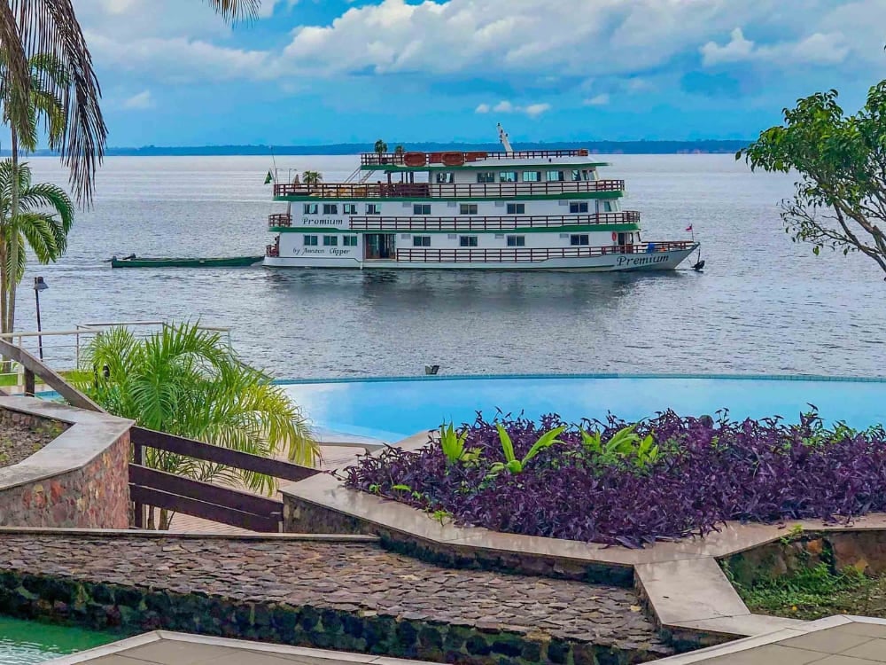 Vue aérienne de l'Amazon Clipper Premium naviguant sur un affluent étroit et sinueux, entouré par la dense forêt tropicale verdoyante. Vue aérienne de l'Amazon Clipper Premium naviguant sur un affluent étroit et sinueux, entouré par la dense forêt tropicale verdoyante.