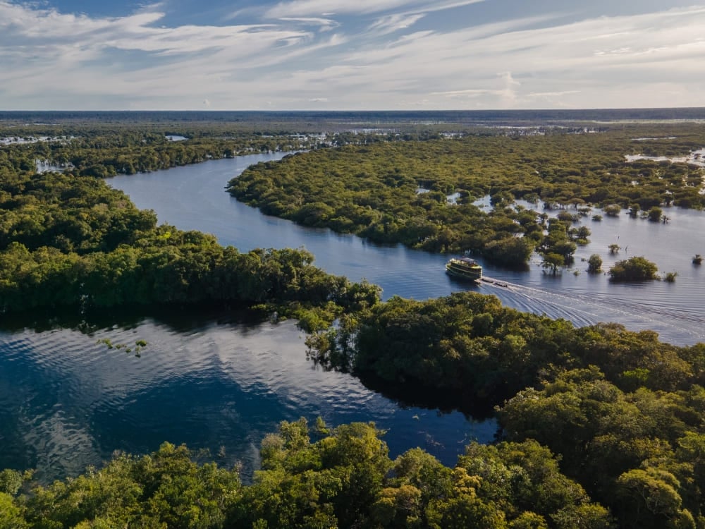 Vue aérienne d'un bateau Katerre naviguant sur les canaux sinueux du Rio Negro lors d'une croisière en Amazonie, entouré d'une végétation verdoyante et luxuriante. Vue aérienne d'un bateau Katerre naviguant sur les canaux sinueux du Rio Negro lors d'une croisière en Amazonie, entouré d'une végétation verdoyante et luxuriante.