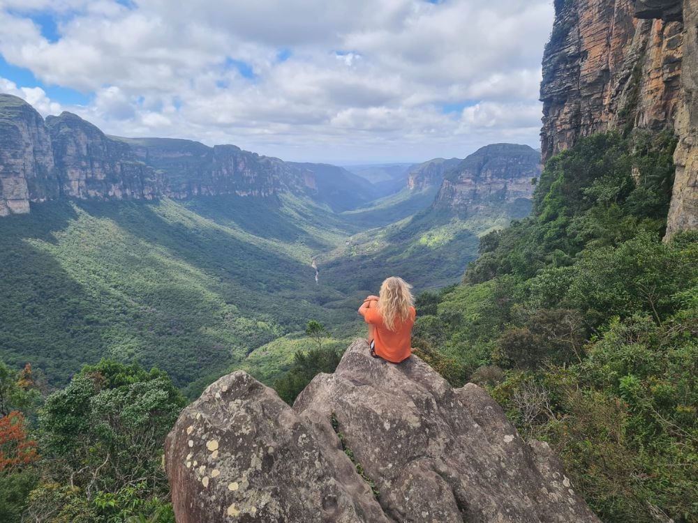 Toerist in een oranje shirt zit op een rotsformatie en kijkt uit over de uitgestrektheid van een groene vallei in Chapada Diamantina Toerist in een oranje shirt zit op een rotsformatie en kijkt uit over de uitgestrektheid van een groene vallei in Chapada Diamantina