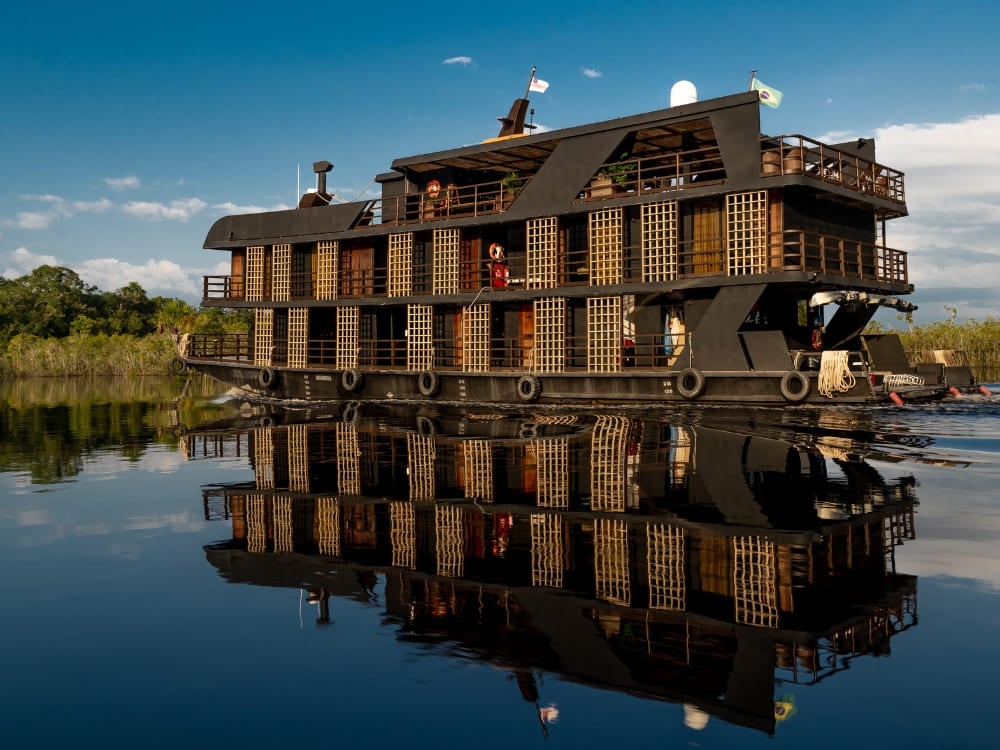 Ein elegantes, mehrstöckiges Schiff spiegelt sich im dunklen Wasser und bietet eine der besten Amazonas-Flusskreuzfahrten in Brasilien. Ein elegantes, mehrstöckiges Schiff spiegelt sich im dunklen Wasser und bietet eine der besten Amazonas-Flusskreuzfahrten in Brasilien.