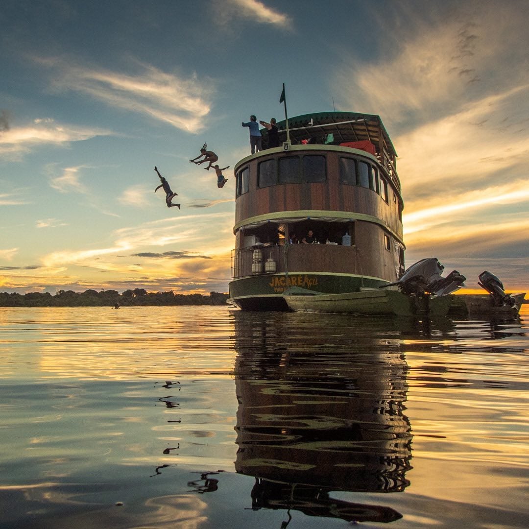 Des touristes plongeant dans le fleuve depuis le pont supérieur du bateau en bois Jacaré-Açu au coucher du soleil lors d'une croisière authentique sur l'Amazone. Des touristes plongeant dans le fleuve depuis le pont supérieur du bateau en bois Jacaré-Açu au coucher du soleil lors d'une croisière authentique sur l'Amazone.