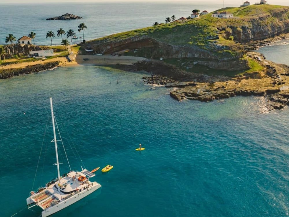 Vue aérienne d'un catamaran blanc ancré dans des eaux cristallines à côté d'une île verdoyante dans l'archipel des Abrolhos. Vue aérienne d'un catamaran blanc ancré dans des eaux cristallines à côté d'une île verdoyante dans l'archipel des Abrolhos.