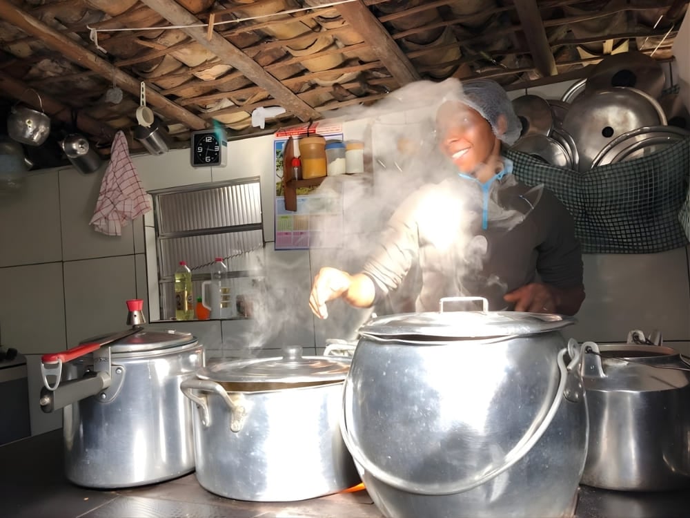 Host cooking with large pots in a rustic kitchen with steam, highlighting the legacy of native women who open the doors of their homes. Host cooking with large pots in a rustic kitchen with steam, highlighting the legacy of native women who open the doors of their homes.