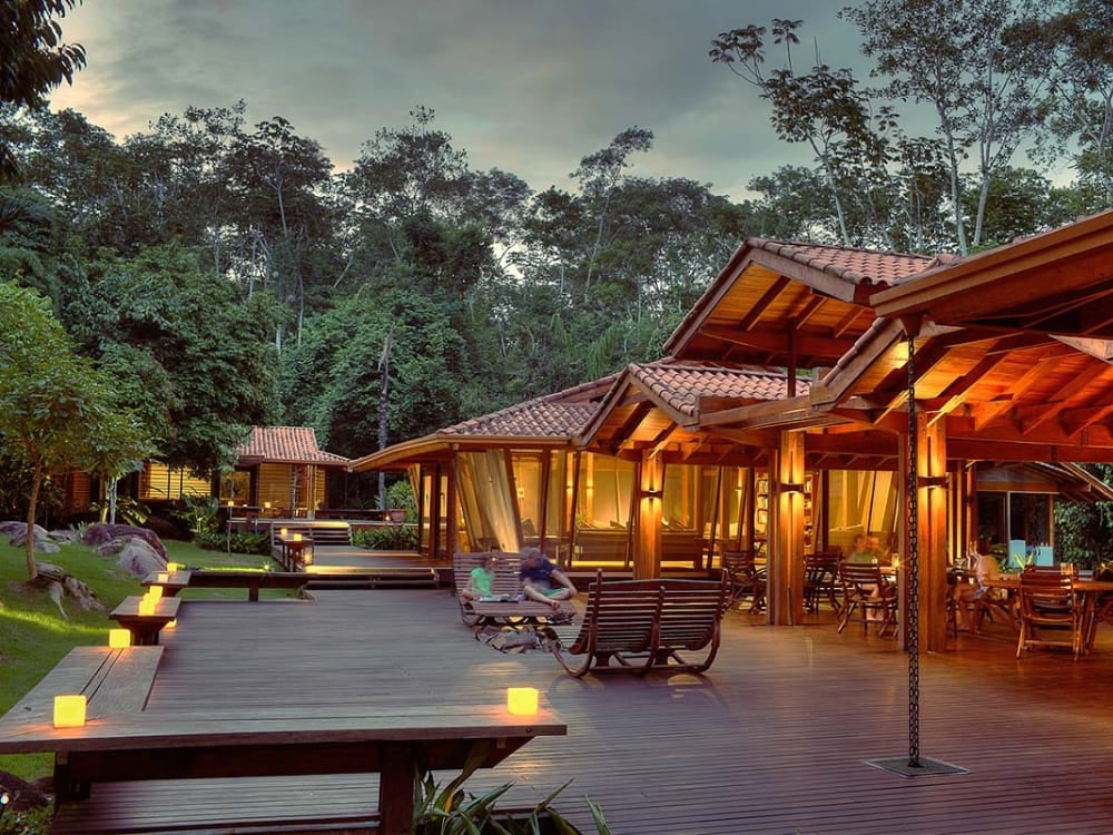 Une terrasse en bois illuminée par de petites lumières au crépuscule, entourée par la végétation tropicale luxuriante de la forêt tropicale. Une terrasse en bois illuminée par de petites lumières au crépuscule, entourée par la végétation tropicale luxuriante de la forêt tropicale.