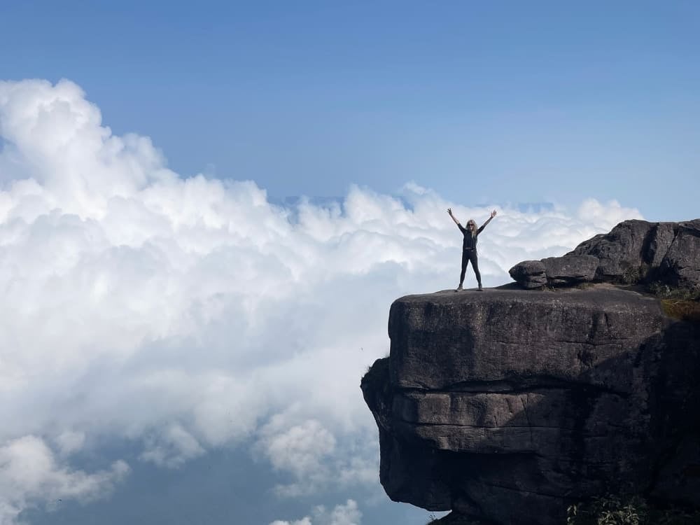 Silhueta de mulher com os braços erguidos em sinal de vitória na beira do penhasco rochoso do Monte Roraima, acima das nuvens brancas. Silhueta de mulher com os braços erguidos em sinal de vitória na beira do penhasco rochoso do Monte Roraima, acima das nuvens brancas.