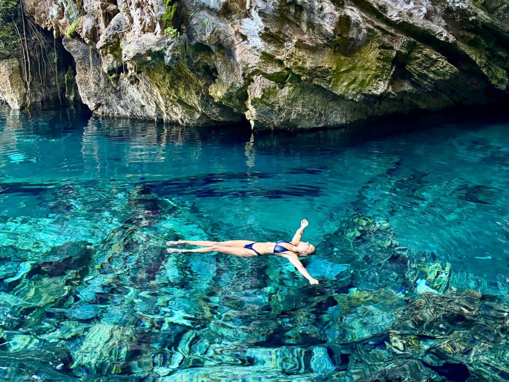Mulher de biquíni flutuando de braços abertos nas águas cristalinas e azul-turquesa de um fervedouro natural cercado por rochas no Jalapão. Mulher de biquíni flutuando de braços abertos nas águas cristalinas e azul-turquesa de um fervedouro natural cercado por rochas no Jalapão.