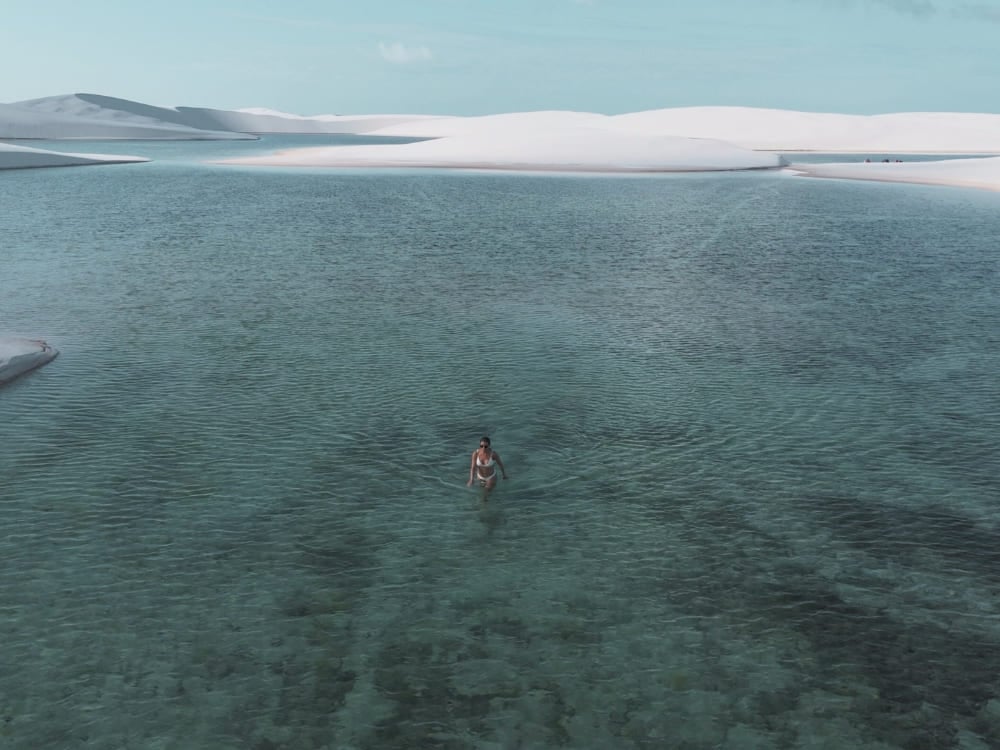 Mulher caminhando nas águas rasas e cristalinas de uma lagoa cercada pelas grandes dunas de areia branca dos Lençóis Maranhenses. Mulher caminhando nas águas rasas e cristalinas de uma lagoa cercada pelas grandes dunas de areia branca dos Lençóis Maranhenses.