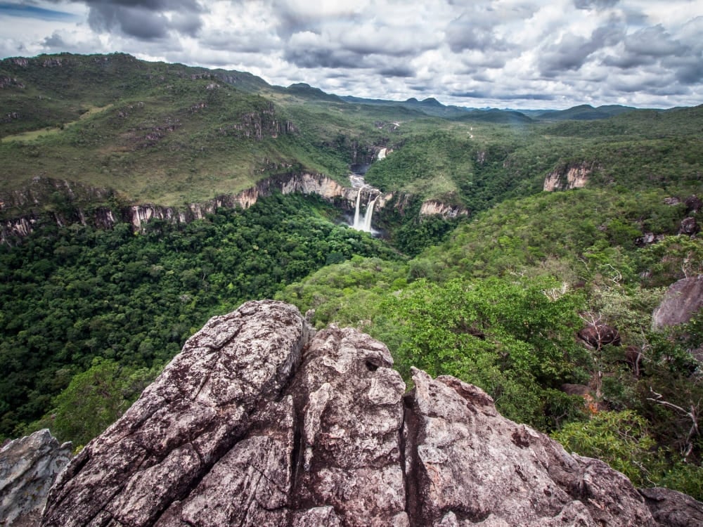 Uitzicht vanaf een rotsachtig uitkijkpunt met in de verte een waterval en weelderige vegetatie in het Nationaal Park Chapada dos Veadeiros. Uitzicht vanaf een rotsachtig uitkijkpunt met in de verte een waterval en weelderige vegetatie in het Nationaal Park Chapada dos Veadeiros.
