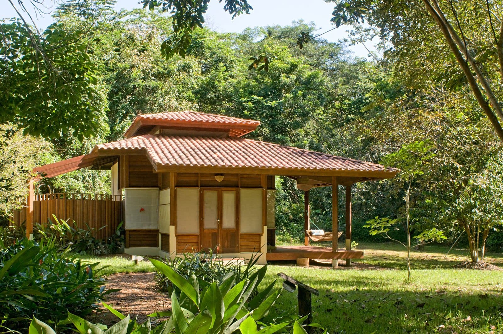 Entre deux sorties ornithologiques à l'aube, la véranda ombragée et son hamac font le reste du travail. Photo: Luis Gomes Bungalow en bois avec toit en tuiles de terre cuite et véranda couverte avec hamac, niché dans la forêt amazonienne dense — hébergement pour l'observation des oiseaux en Amazonie au Cristalino Jungle Lodge