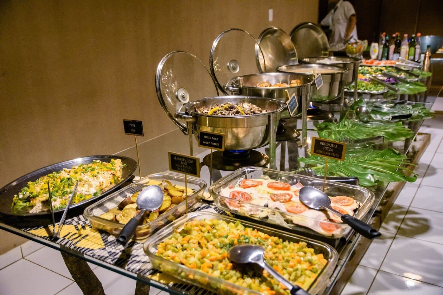 Nach einem langen Tag auf Tierbeobachtung schmeckt das Buffet gleich doppelt gut. Ein reichhaltiges Abend-Buffet in einer Lodge für eine Budget-Pantanal-Tour mit beschrifteten Gerichten wie Süßkartoffel, Auberginenpizza, gemischtem Gemüse, Fisch und frischen Salaten in Warmhaltebehältern