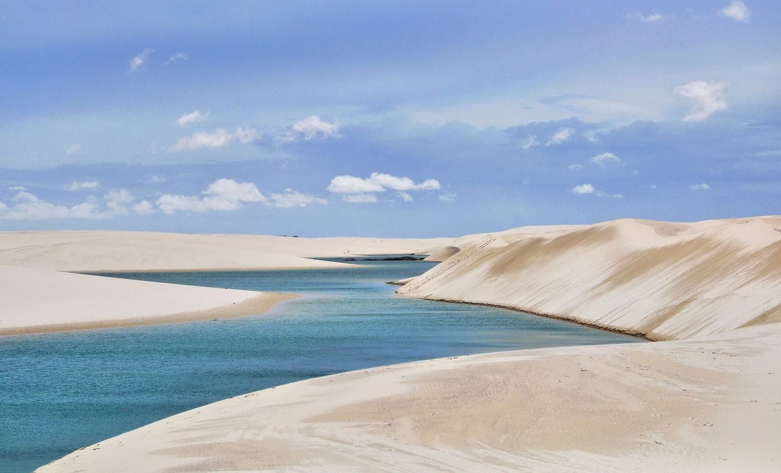 Água doce entre dunas brancas: a natureza fazendo o que sabe de melhor. Lagoa de água turquesa encravada entre dunas de areia branca sob céu azul nos Lençóis Maranhenses