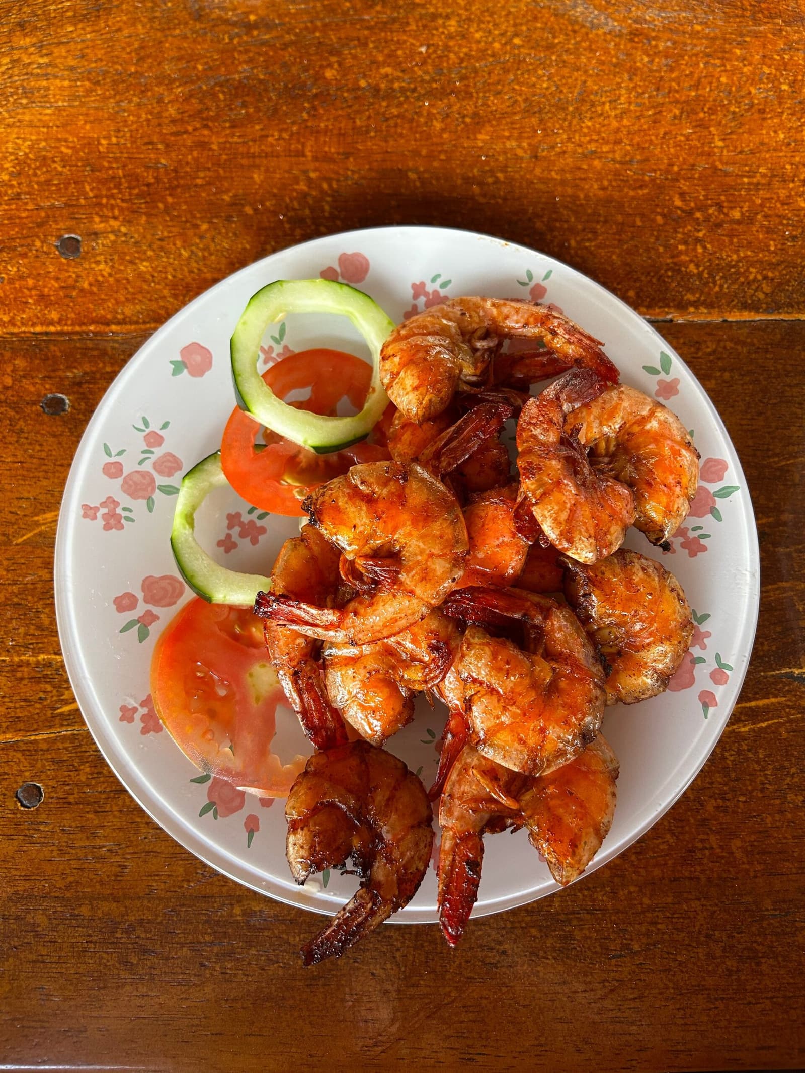 Le genre d'assiette qui repousse toutes les visites de l'après-midi. Vue de dessus d'une assiette de crevettes entières grillées accompagnées de tomates et de concombre en rondelles sur un plat à motifs floraux, servi dans un restaurant local près de Lençóis Maranhenses