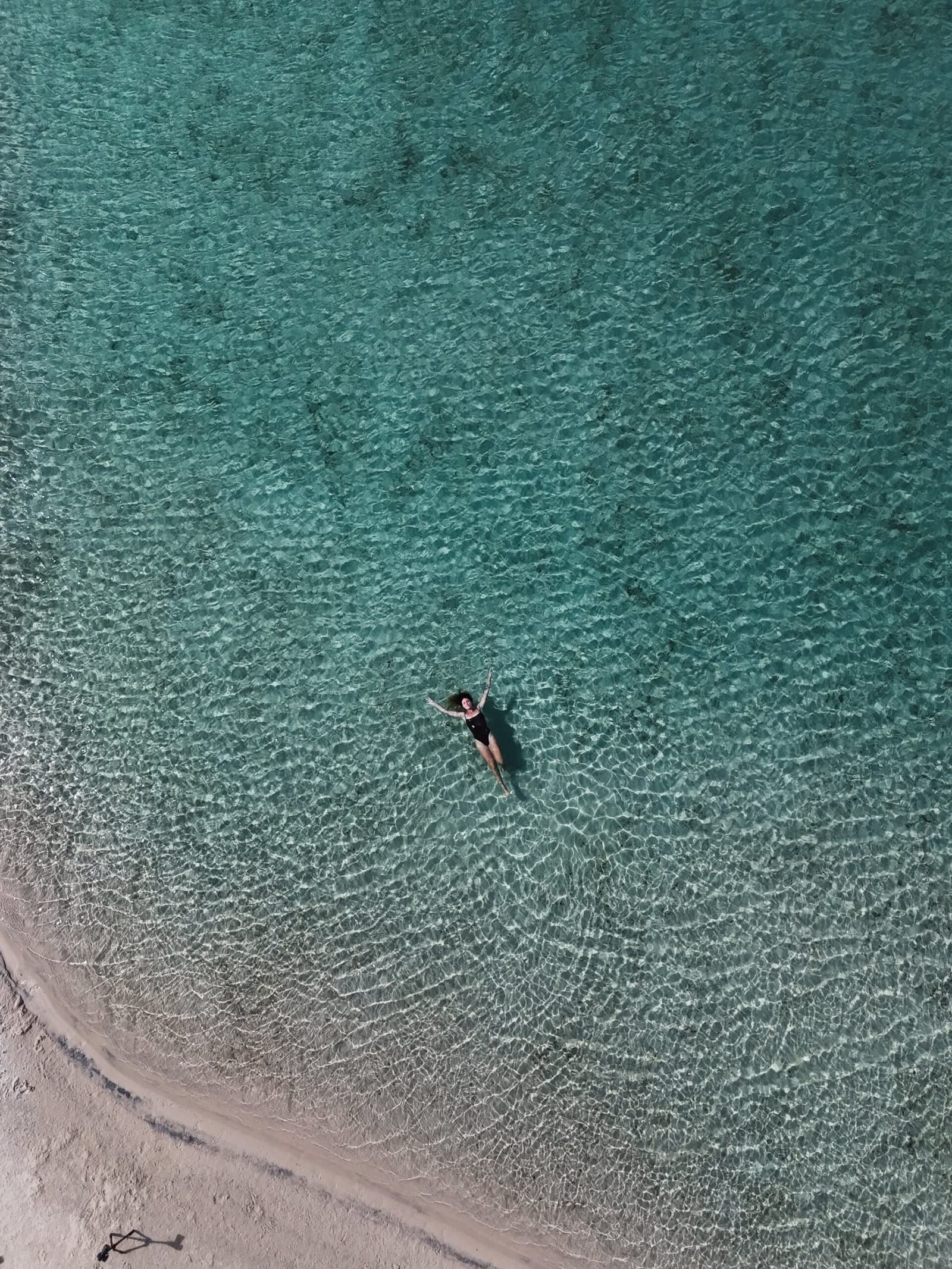 De l'eau tiède, du sable blanc, et rien d'autre à faire. Vue aérienne par drone d'une femme flottant sur le dos dans une eau turquoise cristalline près d'une rive de sable blanc lors d'un trek dans les Lençóis Maranhenses