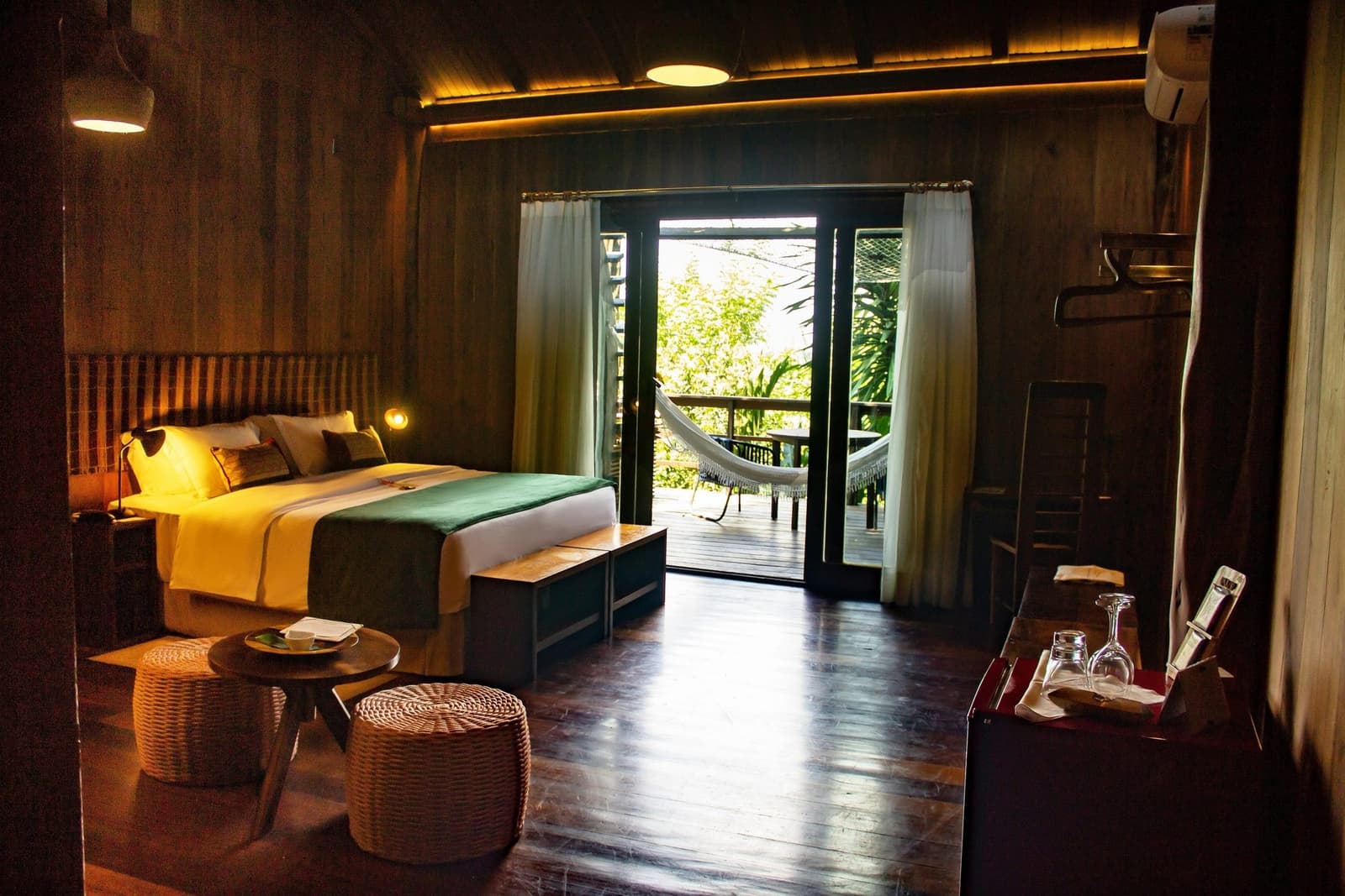 Un hamac, la canopée au bout du balcon, et une bonne raison de ne rien planifier. Chambre en bois chaleureusement éclairée au Mirante do Gavião, avec un grand lit aux draps jaunes et verts, des poufs en osier et des portes-fenêtres ouvertes sur un balcon privé équipé d'un hamac face à la canopée