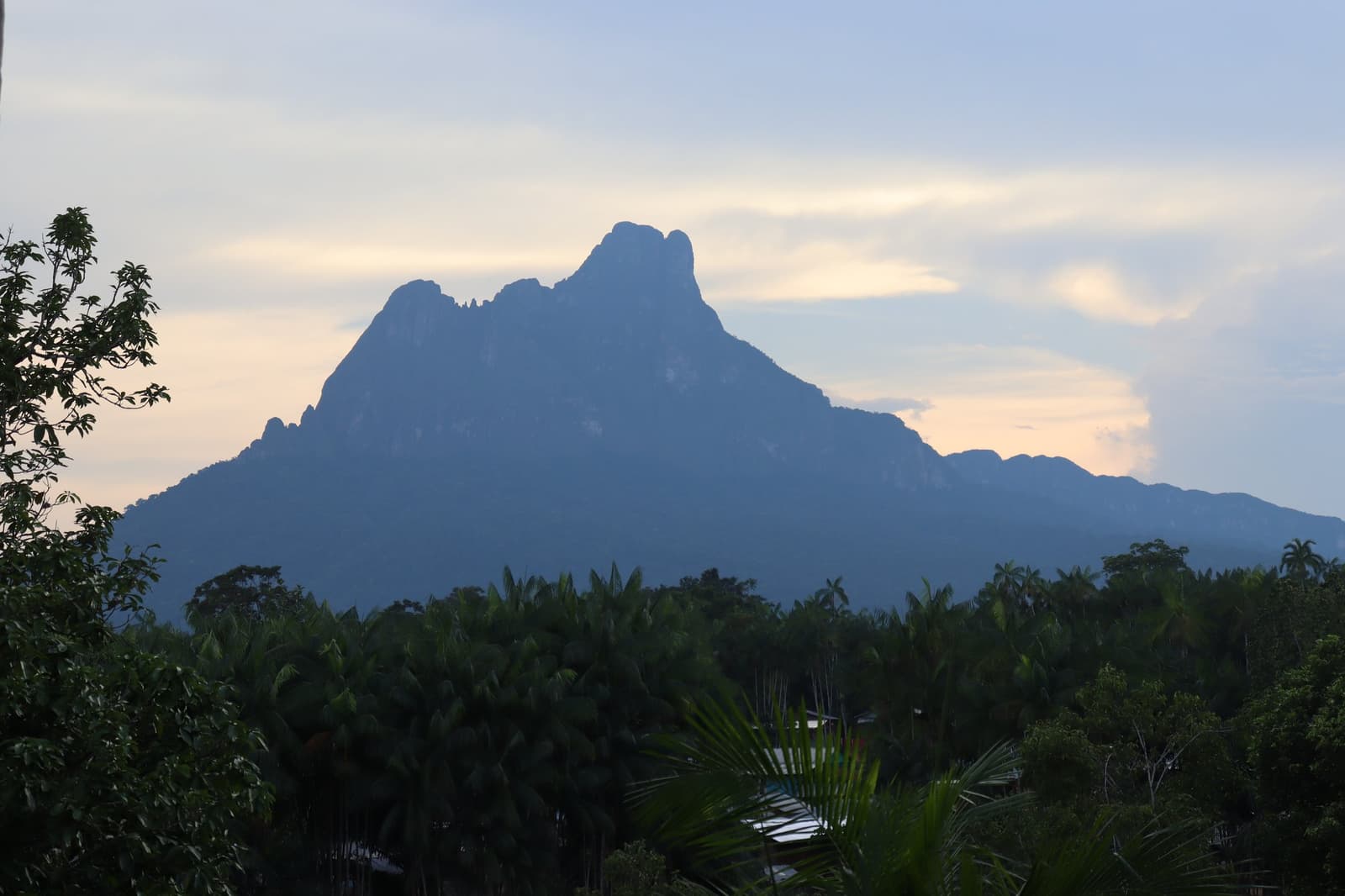Die top houdt al wacht over het woud lang voordat iemand eraan dacht hem te beklimmen. Gekartelde rotsachtige top van de Pico da Neblina die bij schemering boven het dichte Amazoneregenwoud uittorent, als silhouet tegen een zacht blauw en perzikkleurige lucht