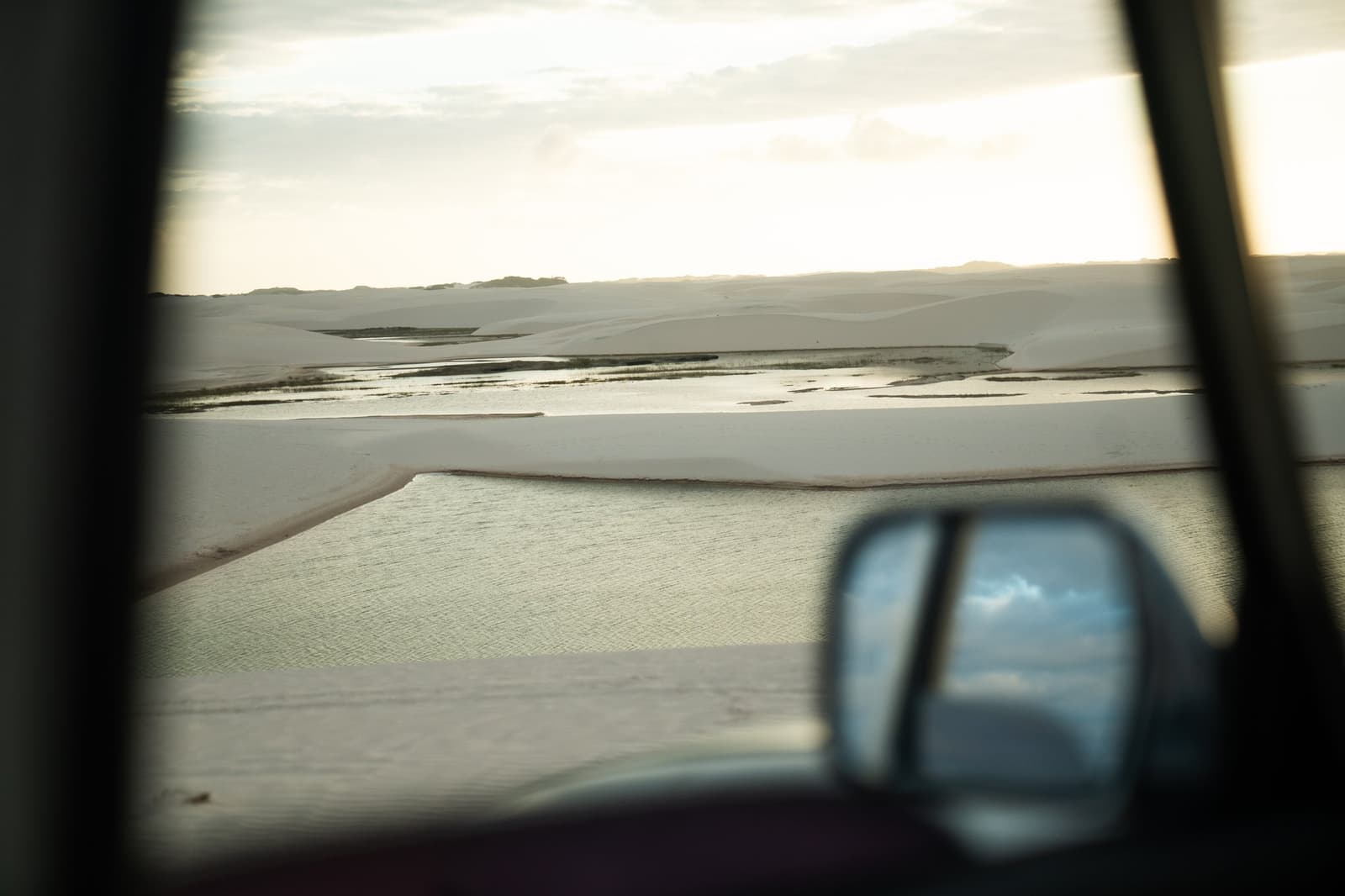 Les dunes s'annoncent avant même que la portière soit ouverte. Dunes de sable blanc et lagunes peu profondes de Lençóis Maranhenses Santo Amaro vues depuis la fenêtre d'un 4x4, avec le rétroviseur latéral reflétant un ciel nuageux