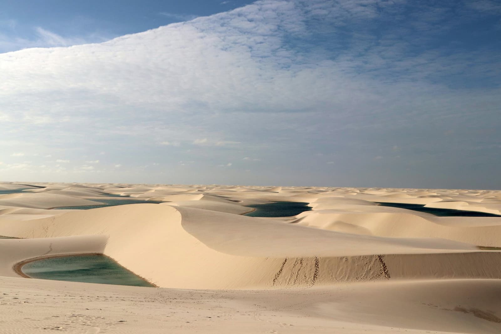 Du sable à perte de vue, et puis ces petites lagunes qui surgissent entre les crêtes. Les immenses dunes de sable blanc des Lençóis Maranhenses s'étendent jusqu'à l'horizon, avec plusieurs lagunes d'eau de pluie turquoise et vertes nichées entre les crêtes sous un vaste ciel bleu