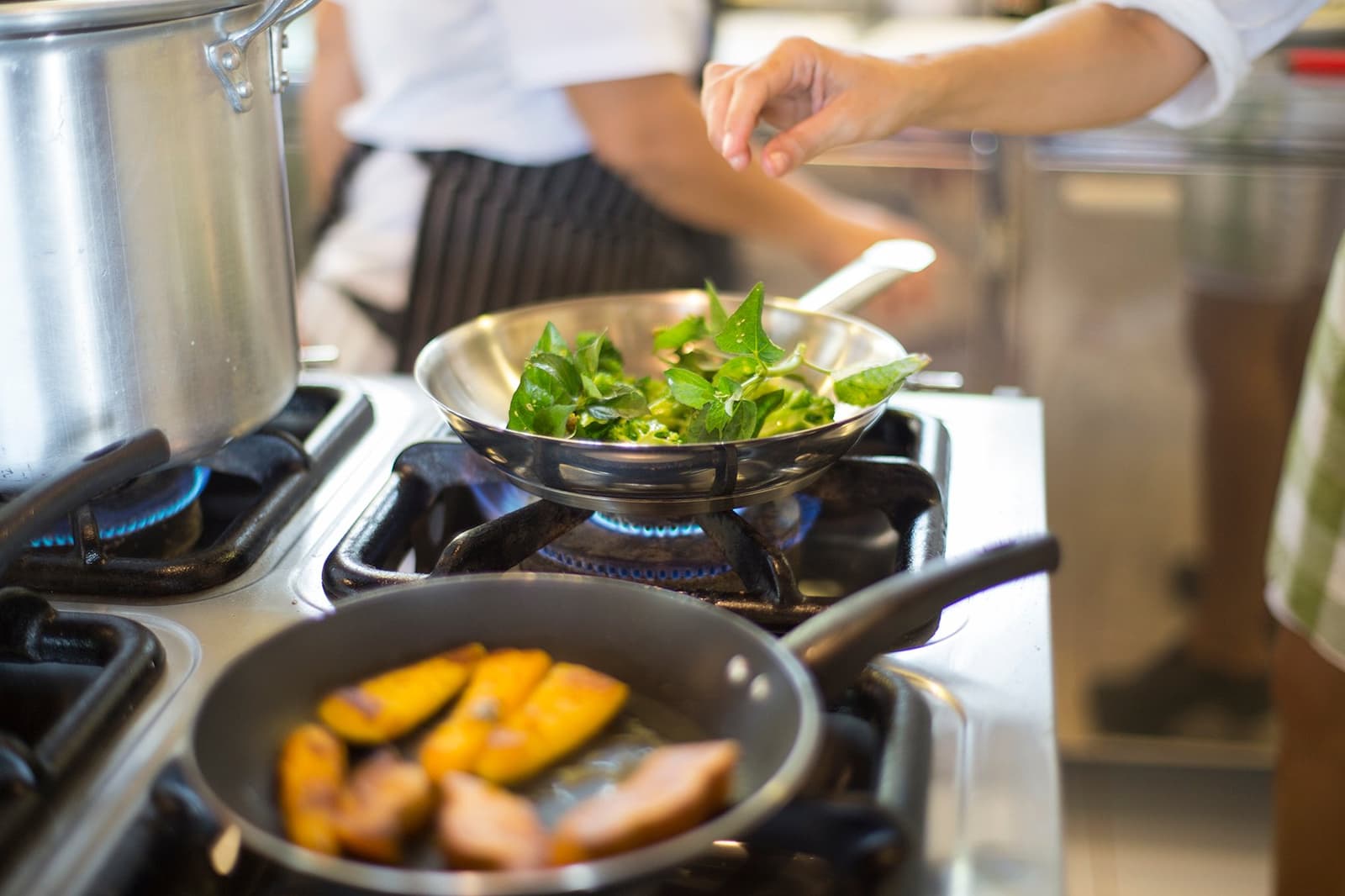 Quand le dîner rivalise avec le coucher de soleil sur le fleuve. Un chef en tablier rayé fait sauter des feuilles vertes fraîches dans une poêle en acier inoxydable sur une flamme à gaz dans la cuisine du lodge Mirante do Gavião, tandis que des tranches de fruits dorées cuisent dans une seconde poêle au premier plan