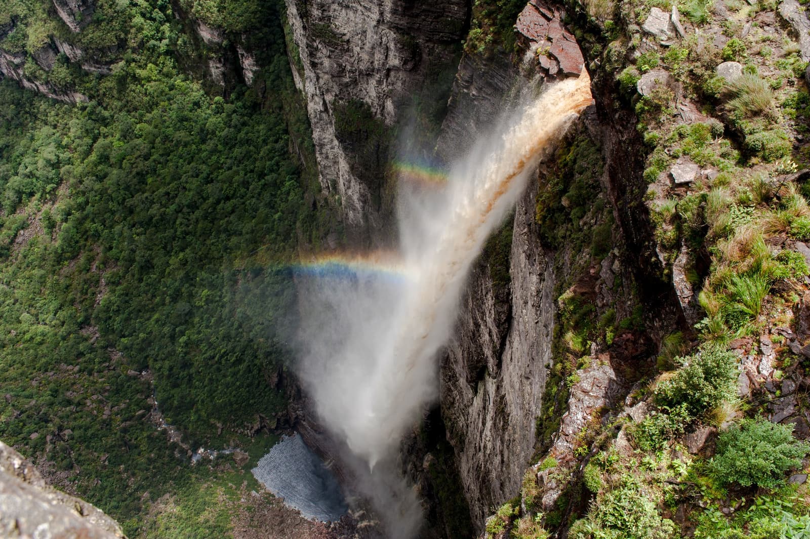 Un arc-en-ciel au milieu de la chute, pas en décoration, en plein vol. Vue aérienne plongeante sur la cascade Cachoeira da Fumaça lors d'un tour Chapada Diamantina, avec un arc-en-ciel formé dans les embruns alors que l'eau chute 380 mètres dans un canyon rocheux bordé de végétation verte