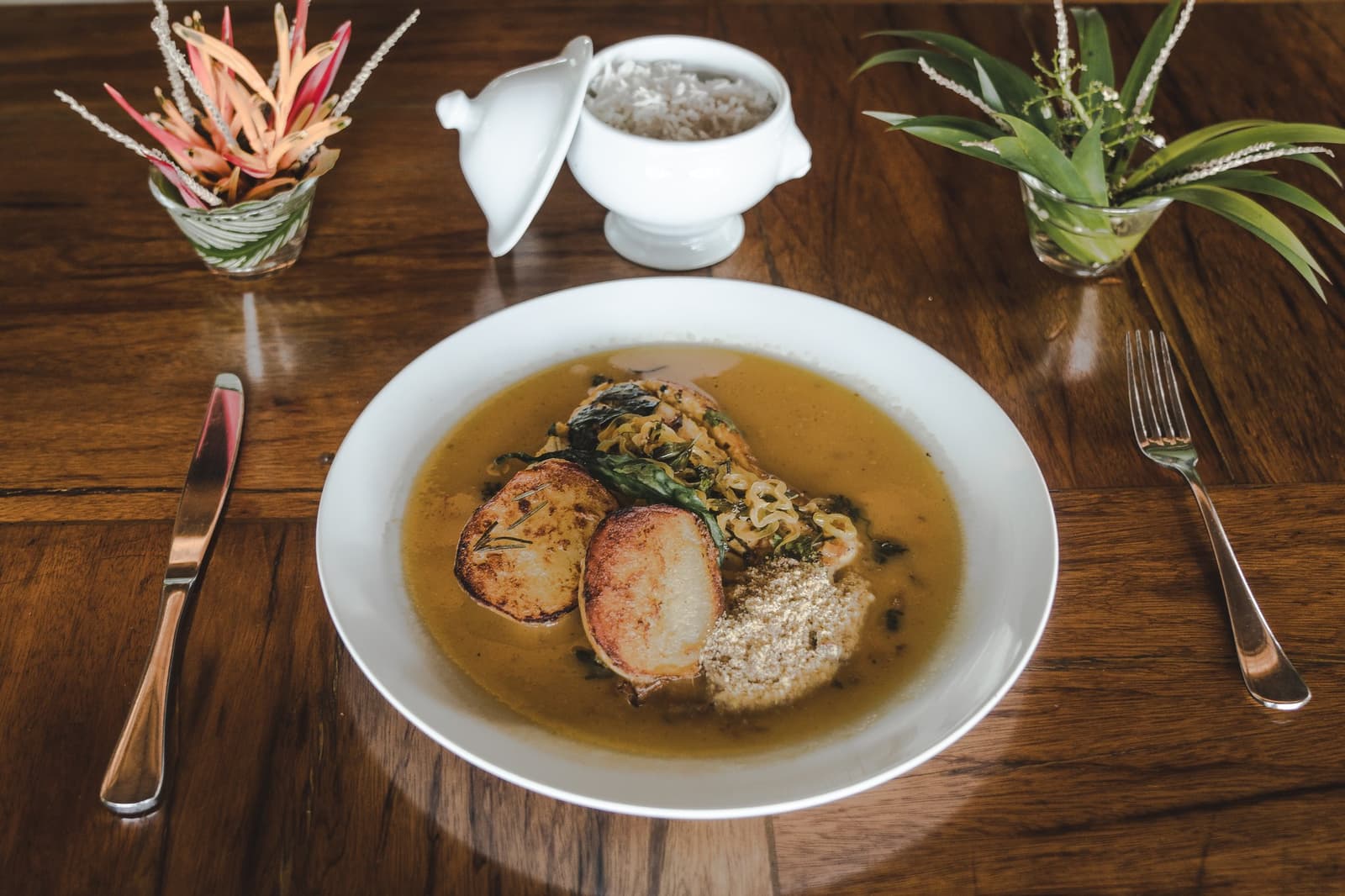 La forêt dans l'assiette, avec toute l'attention qu'elle mérite. Un bol blanc de viande braisée dans un bouillon doré avec des légumes verts sautés, des tranches de pain grillé et de la farine de manioc, servi au restaurant de Mirante do Gavião avec une soupière de riz et des plantes tropicales sur une table en bois poli